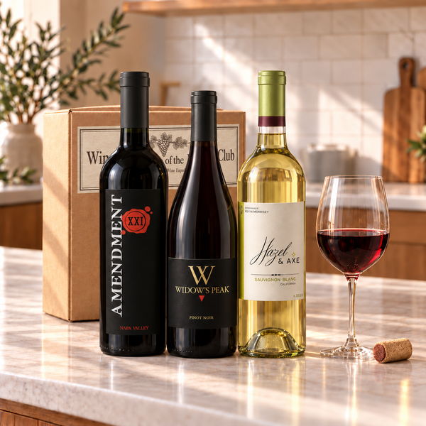 Illustrative 3-bottle mixed red and white wine selection on marble with Wine of the Month Club branded shipping box behind the bottles