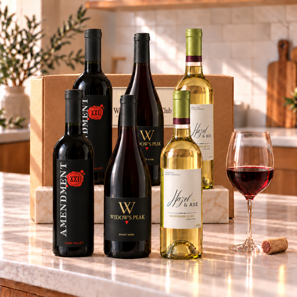 Illustrative 6-bottle mixed red and white wine selection on a rectangular marble platform with a branded shipping box behind the bottles