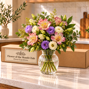Illustrative bouquet in a decorative vase beside an elongated Flower of the Month Club branded shipping box