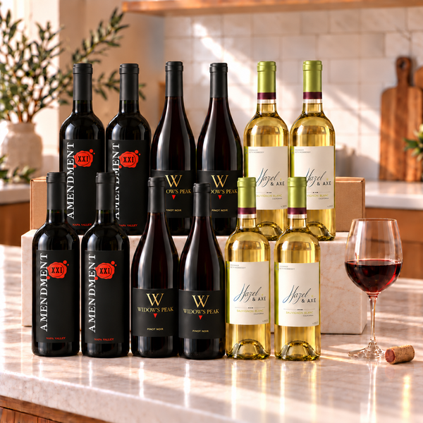 Illustrative 12-bottle mixed red and white wine selection on a rectangular marble platform with a branded shipping box behind the bottles