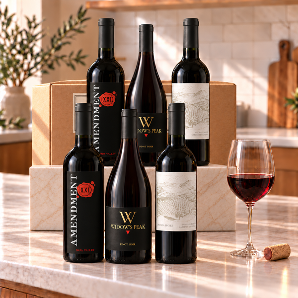 Illustrative six-bottle red wine selection on a rectangular marble platform with a branded shipping box behind the bottles