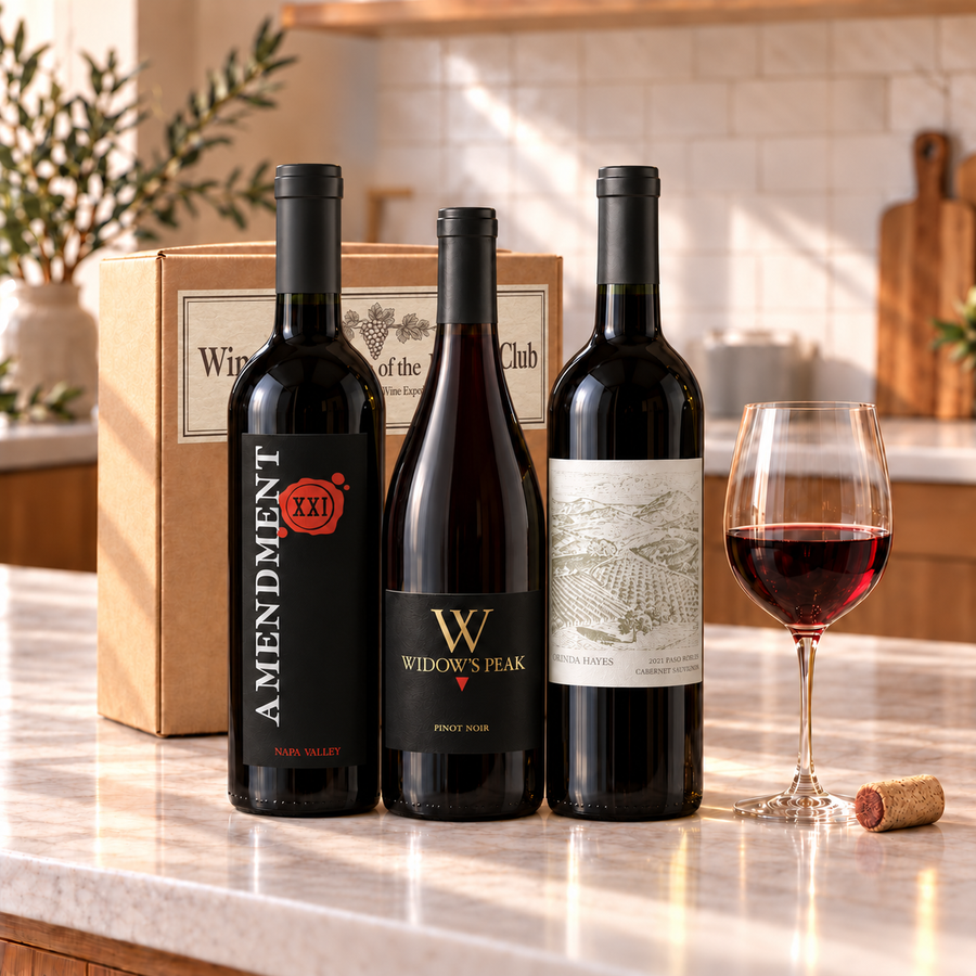Illustrative three-bottle red wine selection on marble with Wine of the Month Club branded shipping box behind the bottles